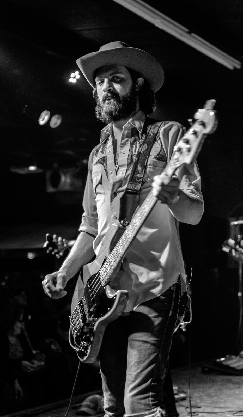 Black and white photograph of a bass player in a cowboy hat at a club show