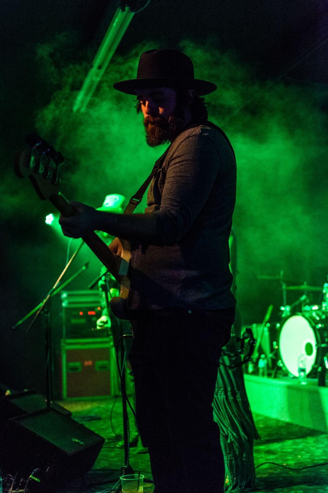 Guitarist in a hat silhouetted in green stage light and smoke